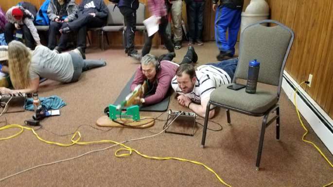 Michael wearing headphones and laying on the floor practicing biathalon rifle shooting