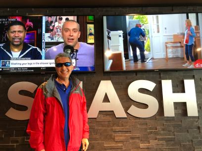 Michael standing in front of Smash Burger sign with two big-screen TVs in the background in Denver Airport