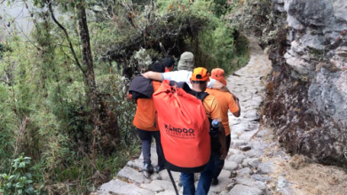 Michael with arms draped over two porters shoulders hiking down the mountain